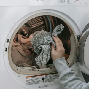 Crop unrecognizable female loading dirty clothes in modern white washing machine while doing housework routine in light room at home