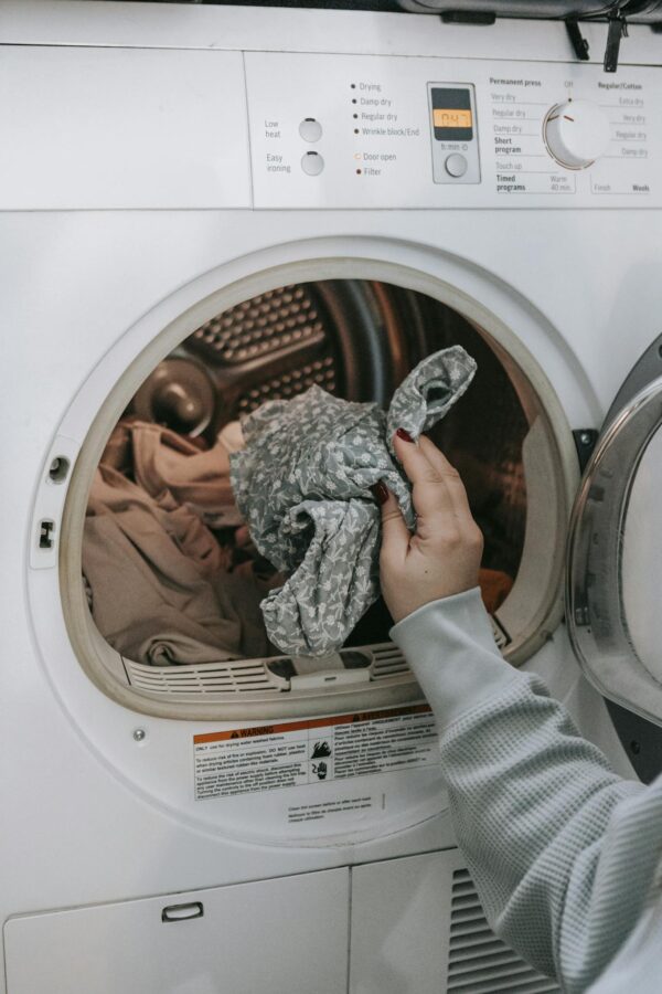 Crop unrecognizable female loading dirty clothes in modern white washing machine while doing housework routine in light room at home