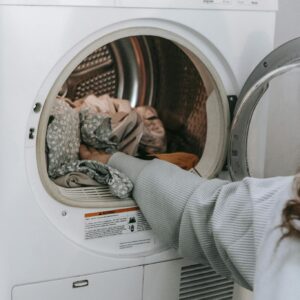 Crop unrecognizable female loading various dirty clothes in modern white washing machine during laundry routine in light room at home