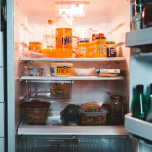 Jars with drinks and containers with preserved food on shelves in fridge at home