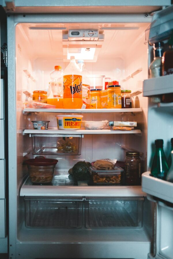 Jars with drinks and containers with preserved food on shelves in fridge at home